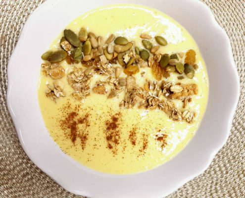 yellow mango banana smoothie in a bowl with granola, see and coconut topping